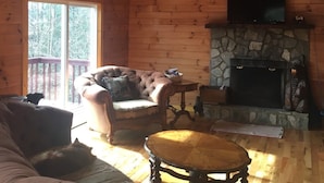 A cozy cabin interior with a stone fireplace, wooden walls, a comfortable sofa, and a television mounted above the fireplace.