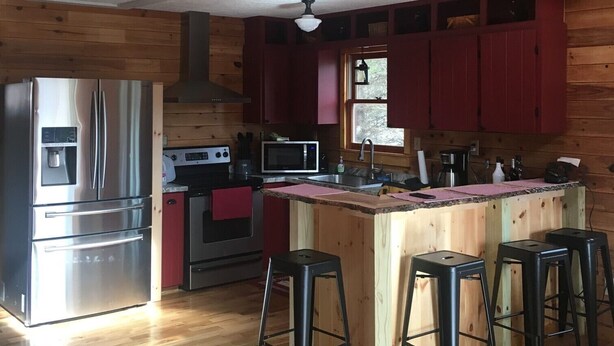 A compact kitchen with wooden walls, a stainless steel refrigerator, a microwave, a stove, and a wooden island with stools.