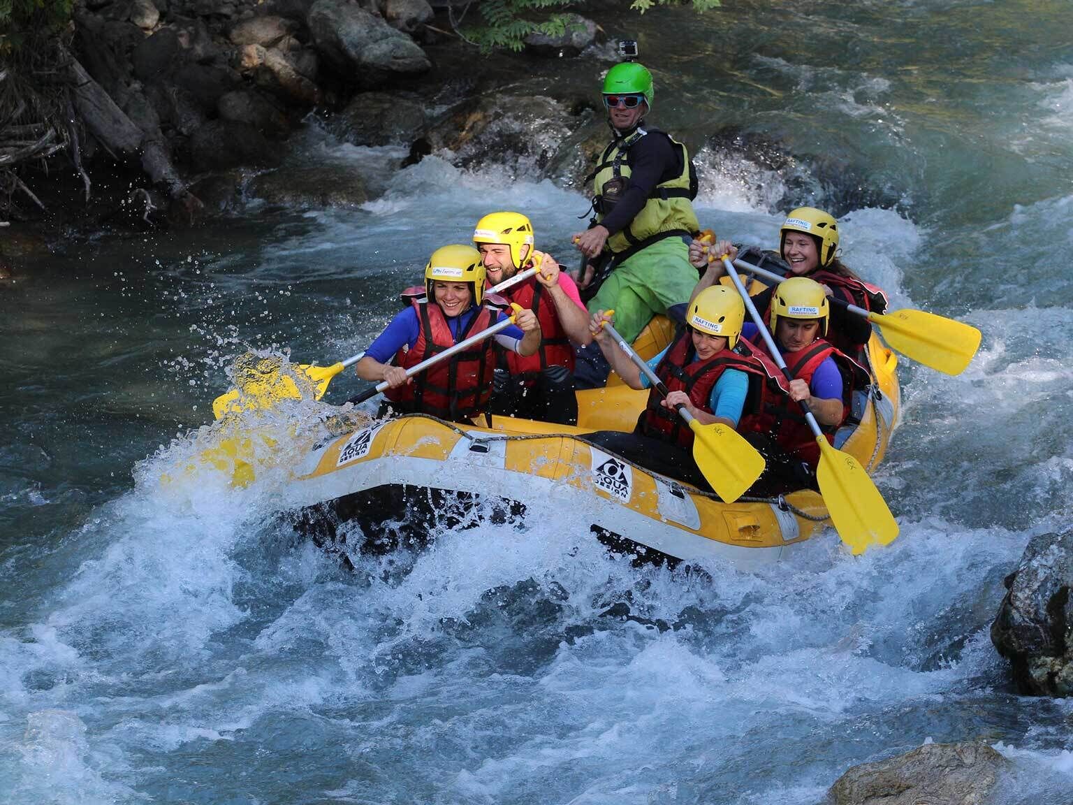 A group of people in a yellow raft navigating a river with rapids.
