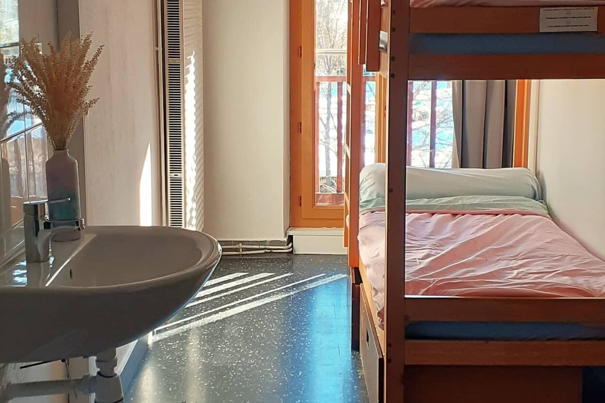 Ein Zimmer mit einem Etagenbett, einem Waschbecken, einem Fenster und einer Heizung.