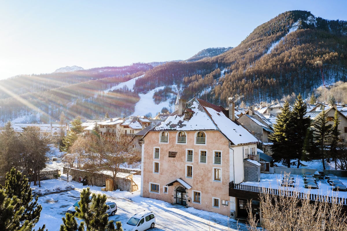Ein Gebäude mit schneebedecktem Dach, umgeben von Bäumen und einer Bergkulisse.