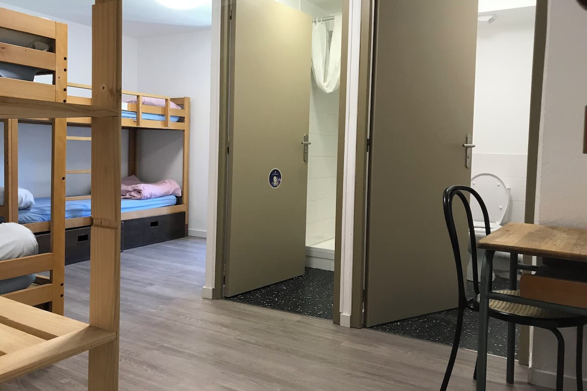 Ein Zimmer mit Etagenbetten, Dusche, Toilette und einem Esstisch mit Stühlen.
