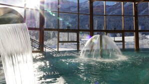 A hot spring area with a waterfall, large windows, and a view of snow-covered mountains.