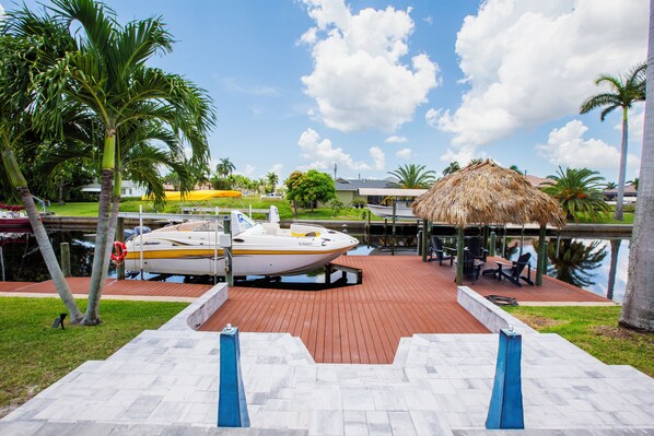 A boat docked at a pier with a thatched-roof structure nearby. - Waterfront Paradise: Gulf Access Pool Home + Boat Rental Option! (Cape Coral)