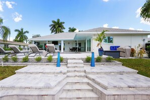 A modern house with a covered patio, outdoor seating, and a well-maintained lawn. - Waterfront Paradise: Gulf Access Pool Home + Boat Rental Option! (Cape Coral)