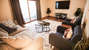 Un salon comprenant un canapé, des fauteuils, une table basse, un téléviseur et une porte-fenêtre coulissante.