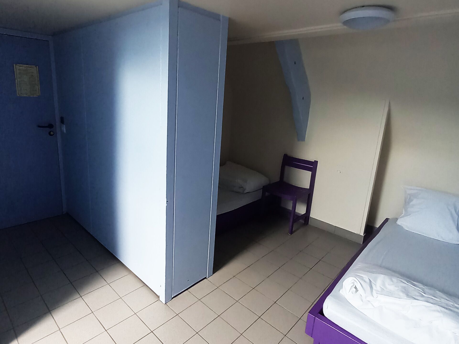 A small room with a bed, a chair, and a door.