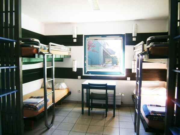 Un dormitorio con literas, un escritorio y una ventana que da a un edificio.