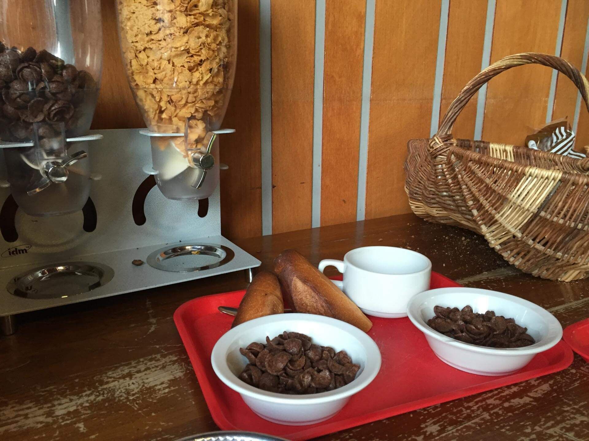 Une machine à café qui verse du café dans une tasse, deux bols remplis de pépites de chocolat et un panier en osier sur une table en bois.