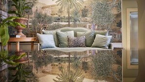 Quarto com sofá verde, planta em vaso e painel com paisagem tropical.