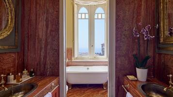 Een luxe badkamer met een vrijstaand bad, twee wastafels en een groot raam met uitzicht op zee.