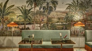 Quarto com um sofá verde, duas mesinhas laterais com velas e um mural de paisagem tropical.