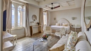 Um quarto espaçoso com uma cama grande, um espaço de estar com um sofá e poltronas, uma mesa de centro de madeira e um ventilador de teto.