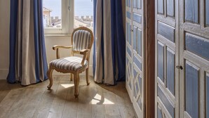 Quarto com uma cadeira de madeira, uma janela ampla com cortinas e uma porta com painéis decorativos.