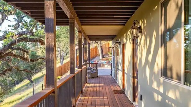 A covered wooden deck with a railing, a bench, and a view of a backyard with trees and a fence. - Z Ranch - Modern French Country Style With Stunning Views (Atascadero)
