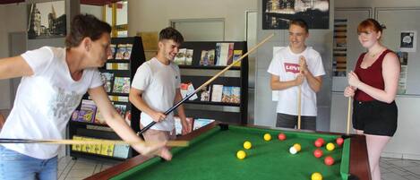 A pool table in a room with bookshelves and a cityscape painting on the wall.