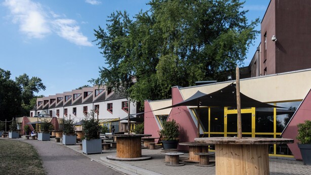 A courtyard with outdoor seating, a building with a modern design, and a large tree providing shade.