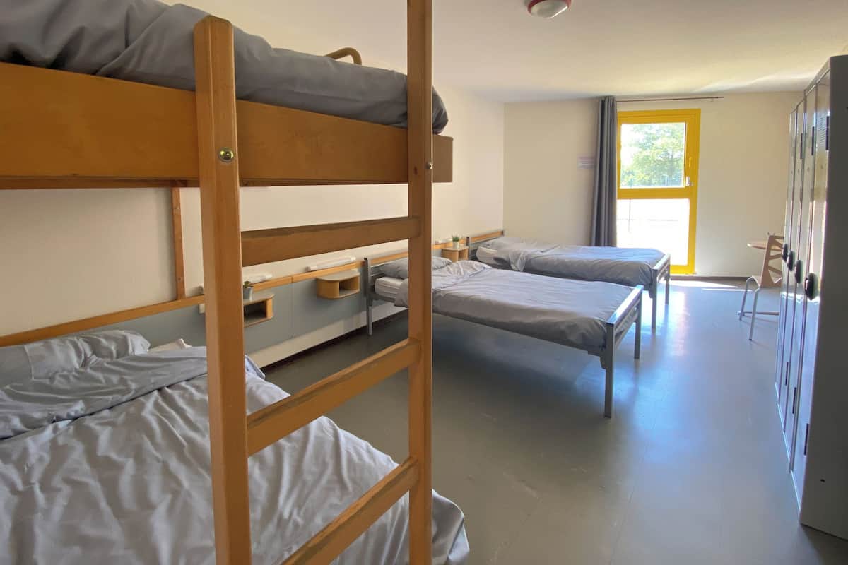 A dormitory room with bunk beds, a small table, and a window.