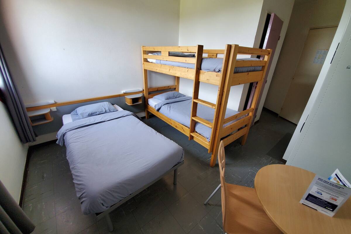 A bunk bed room with a desk and chair, a small shelf, and a door.