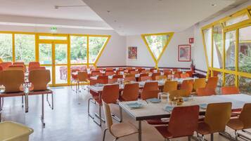 A conference room with tables and chairs, large windows, and a view of greenery outside.