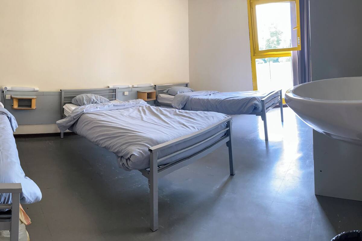 A clinical room with three single beds, each with a bedside table and a lamp. There is a large sink on the right side.