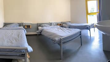 A clinical room with three single beds, each with a bedside table and a lamp. There is a large sink on the right side.