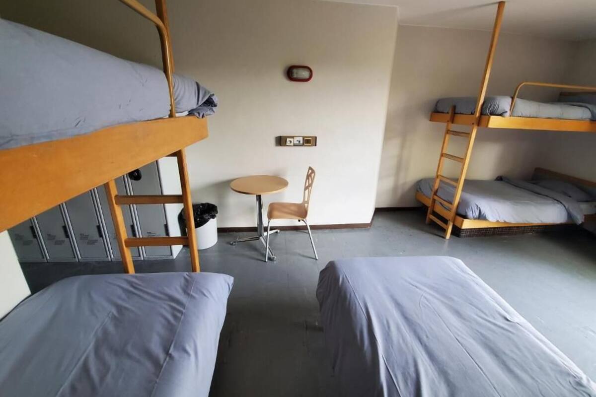 A dormitory room with bunk beds, a small round table, and a chair.