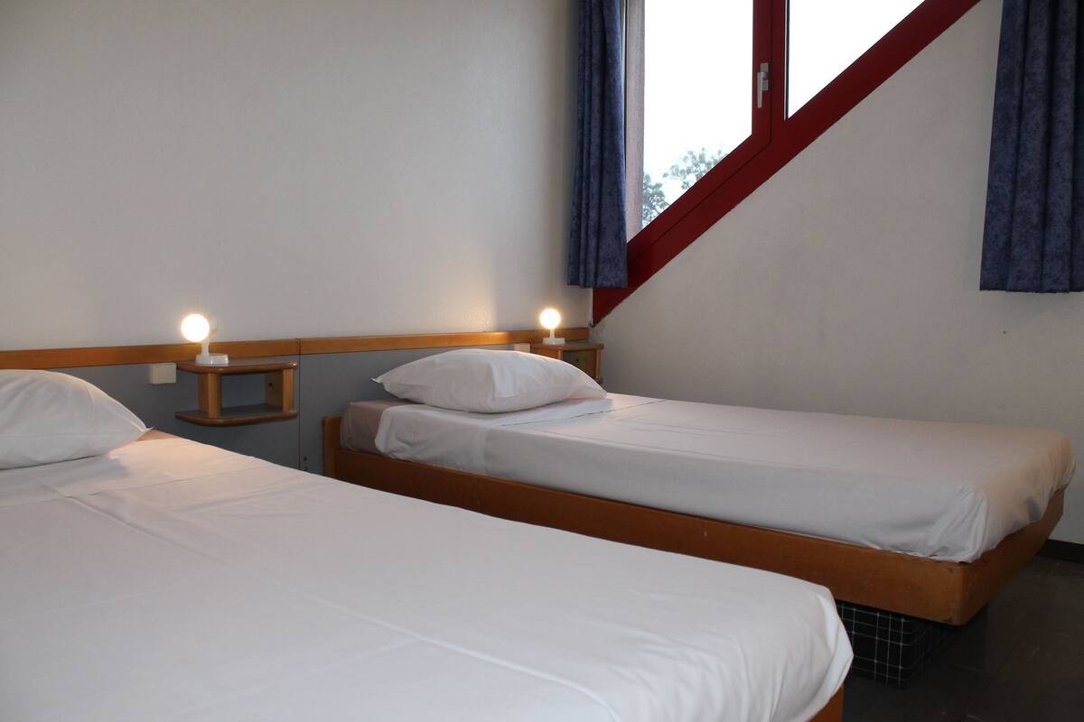 A room with two single beds, each with a wooden headboard and white bedding. There are bedside tables with lamps.