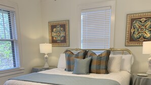 Un dormitorio con una cama grande, dos mesitas de noche y dos ventanas con persianas.