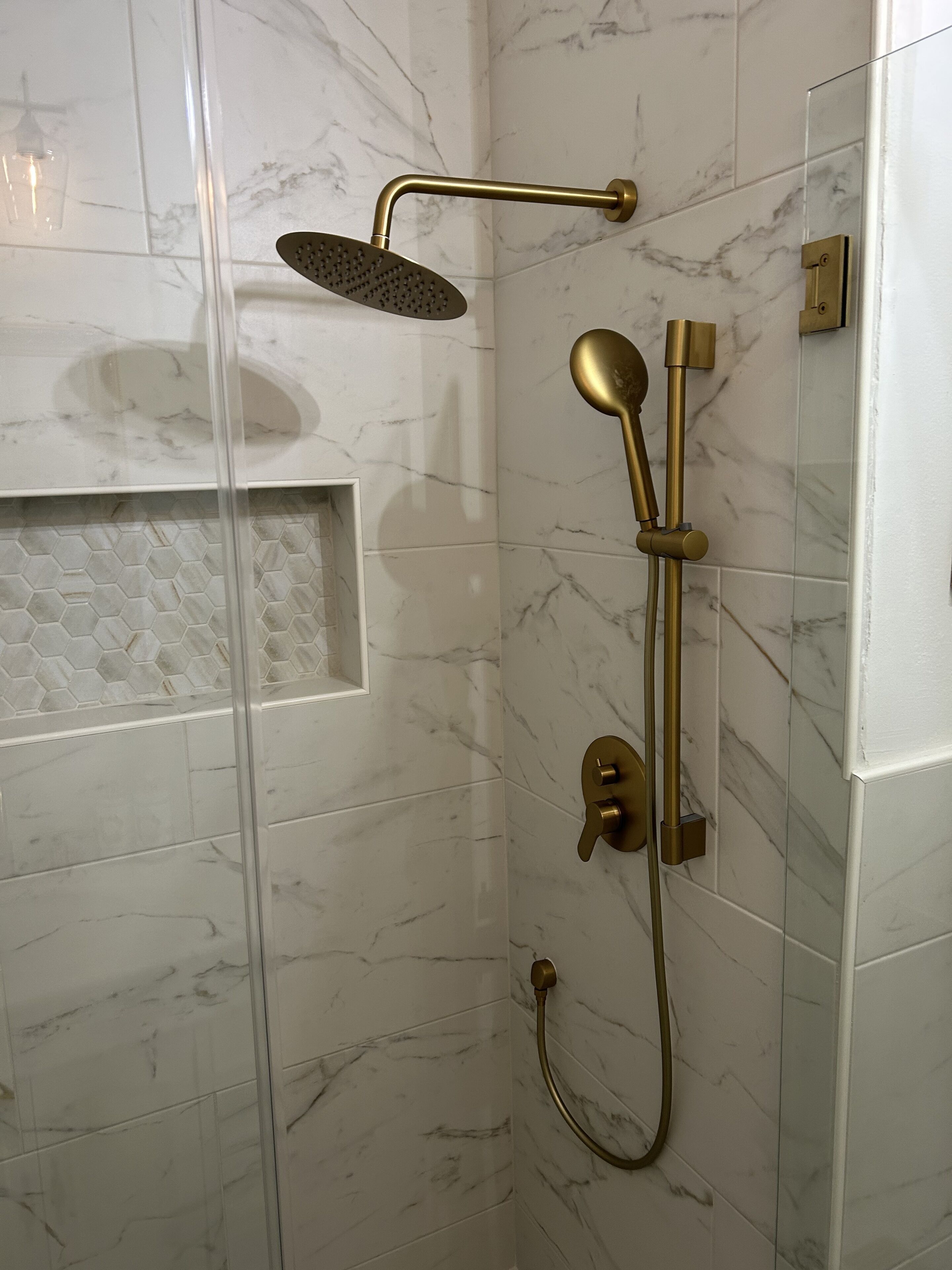 A shower with a glass enclosure, a handheld showerhead, and a wall-mounted control panel.