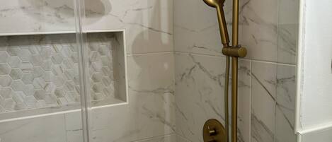 A shower with a glass enclosure, a handheld showerhead, and a wall-mounted control panel.