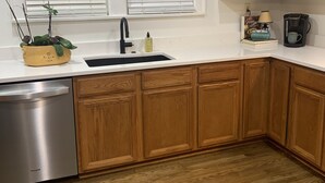 Una cocina con armarios de madera, lavavajillas de acero inoxidable, un lavabo y una ventana con persianas.
