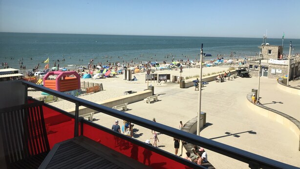 En strand med ett badvakts torn, parasoller och folk.