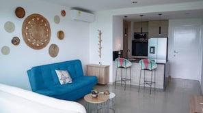 Uma sala de estar moderna com um sofá azul, uma mesinha redonda e uma área de cozinha com dois banquetas.