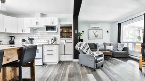 A modern kitchen with white cabinets, a wooden dining table, and a gray sofa in the living area. - Chalet with waterfront, Spa and magnificent view of a regional park (Chertsey)