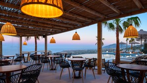 Un espace extérieur aménagé avec des chaises et des tables en osier, offrant une vue sur une piscine et une plage.