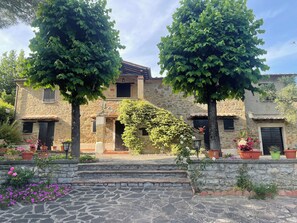 A stone building with a courtyard, featuring a staircase, potted plants, and a tree. - Typical stone cottage with large garden and private parking space (Passignano sul Trasimeno)