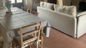 A dining area with a wooden table and chairs, a sofa, and a fireplace. - Typical stone cottage with large garden and private parking space (Passignano sul Trasimeno)