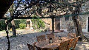 An outdoor wooden table and chairs under a pergola, surrounded by stone walls and greenery. - Typical stone cottage with large garden and private parking space (Passignano sul Trasimeno)