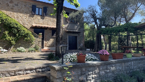 A stone building with a tiled roof, a wooden door, and a small porch with potted plants. - Typical stone cottage with large garden and private parking space (Passignano sul Trasimeno)