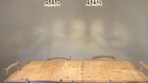 A wooden dining table with six chairs, two hanging pendant lights, and exposed wooden beams on the ceiling. - Typical stone cottage with large garden and private parking space (Passignano sul Trasimeno)