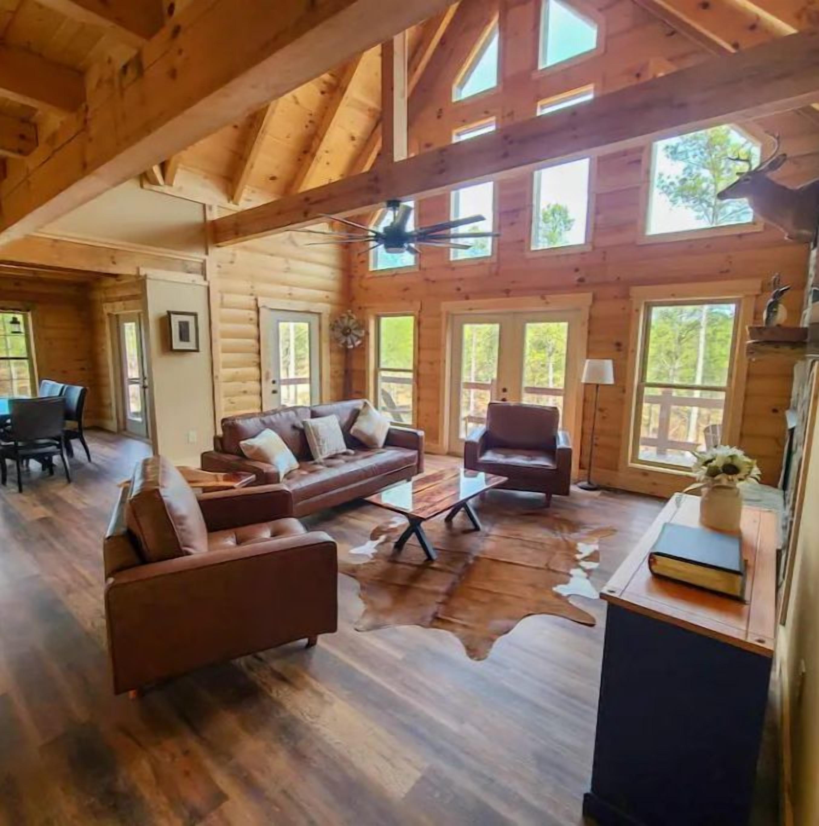 Ein Blockhaushaus-Interieur mit Holzbalkendecke, einem Ledersofa, einem Couchtisch und einem Essbereich.