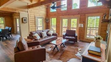 Ein Blockhaushaus-Interieur mit Holzbalkendecke, einem Ledersofa, einem Couchtisch und einem Essbereich.
