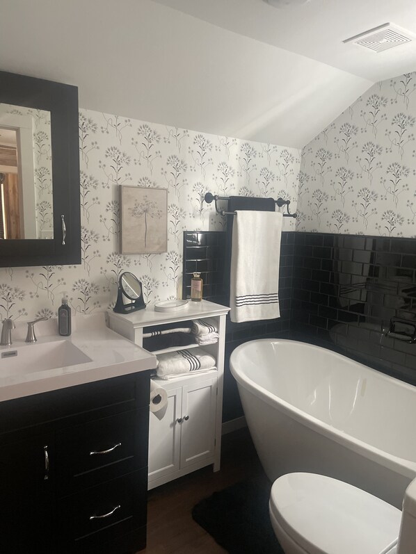 Un baño con un lavabo blanco, un mueble negro y una bañera independiente.