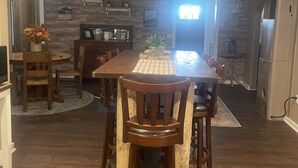 A dining area with a wooden table and chairs, a kitchen with a refrigerator, and a stone wall. - The Pink House - Charming, fully renovated, quiet getaway (Wellfleet)