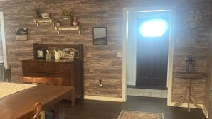 A dining area with a wooden table and chairs, a rug, and a wall with shelves holding decorative items. - The Pink House - Charming, fully renovated, quiet getaway (Wellfleet)