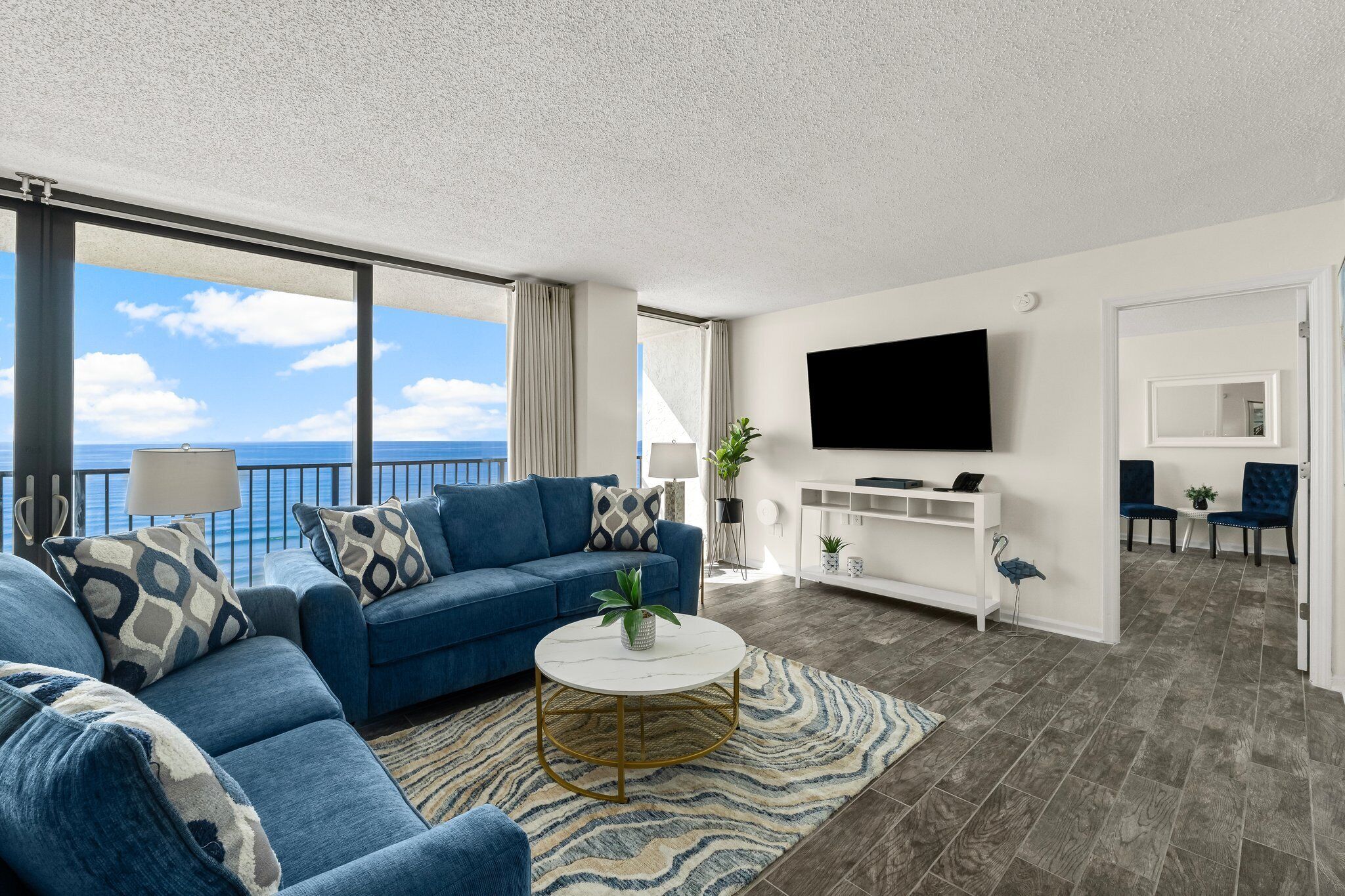A modern living room with a blue sofa, a round coffee table, and a TV mounted on the wall.