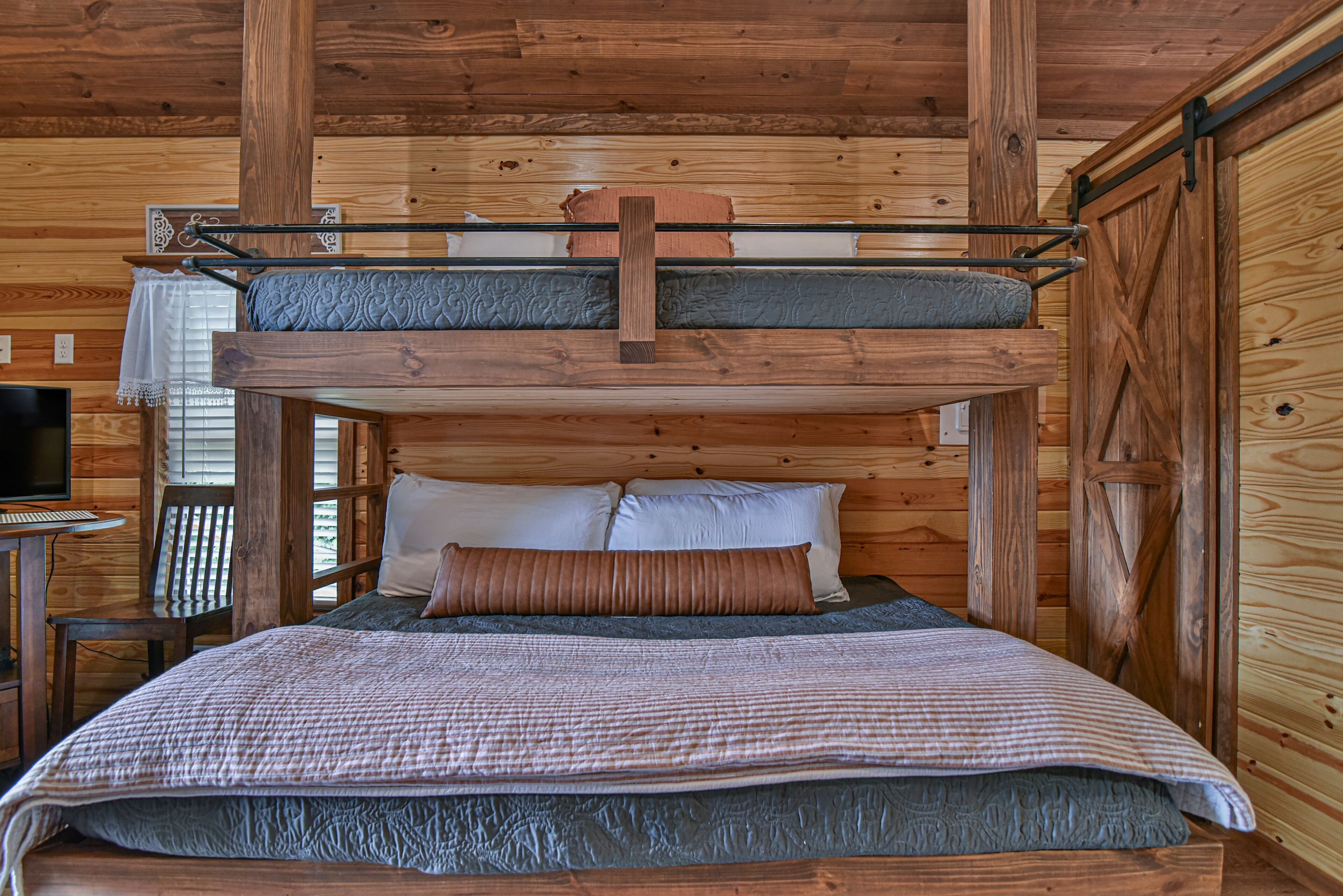 Un lit superposé avec un bureau et une chaise, des murs en bois et un téléviseur.