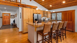 A spacious kitchen with wooden cabinets, a large island with bar stools, and a wooden ceiling. - Enchanting Lindal Waterfront Cabin (Shelton)