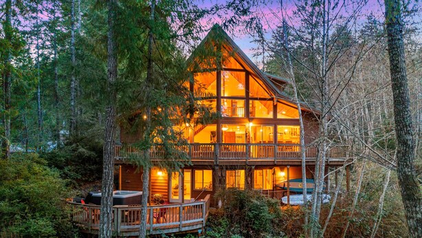 A multi-story log cabin with a deck, surrounded by dense forest. - Enchanting Lindal Waterfront Cabin (Shelton)